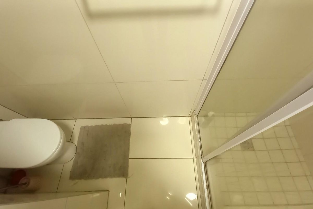 A compact bathroom featuring a toilet and a glass-enclosed shower with neutral tiled walls and flooring.