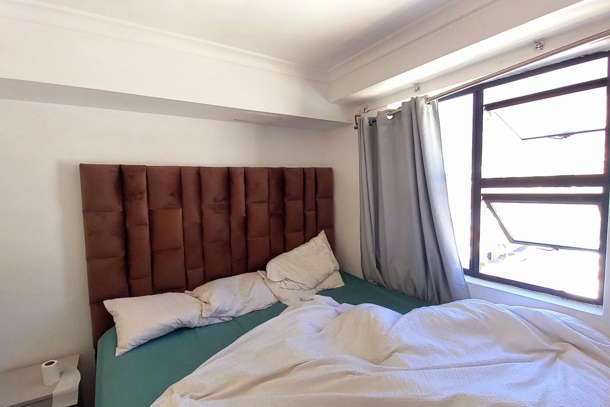 A compact bedroom featuring a large upholstered headboard and a window with natural light, providing a functional sleeping space.