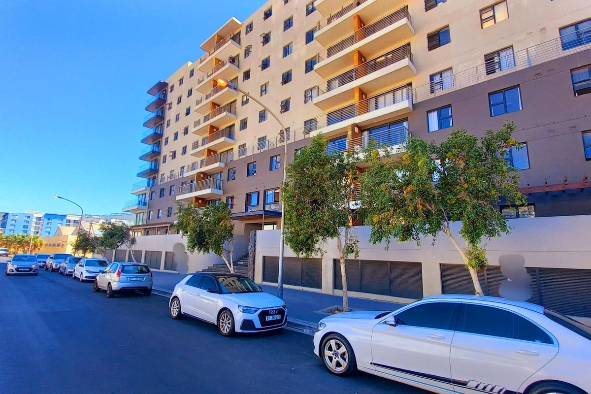 A street-level view of a modern multi-story apartment building featuring private balconies and ground-level parking access.