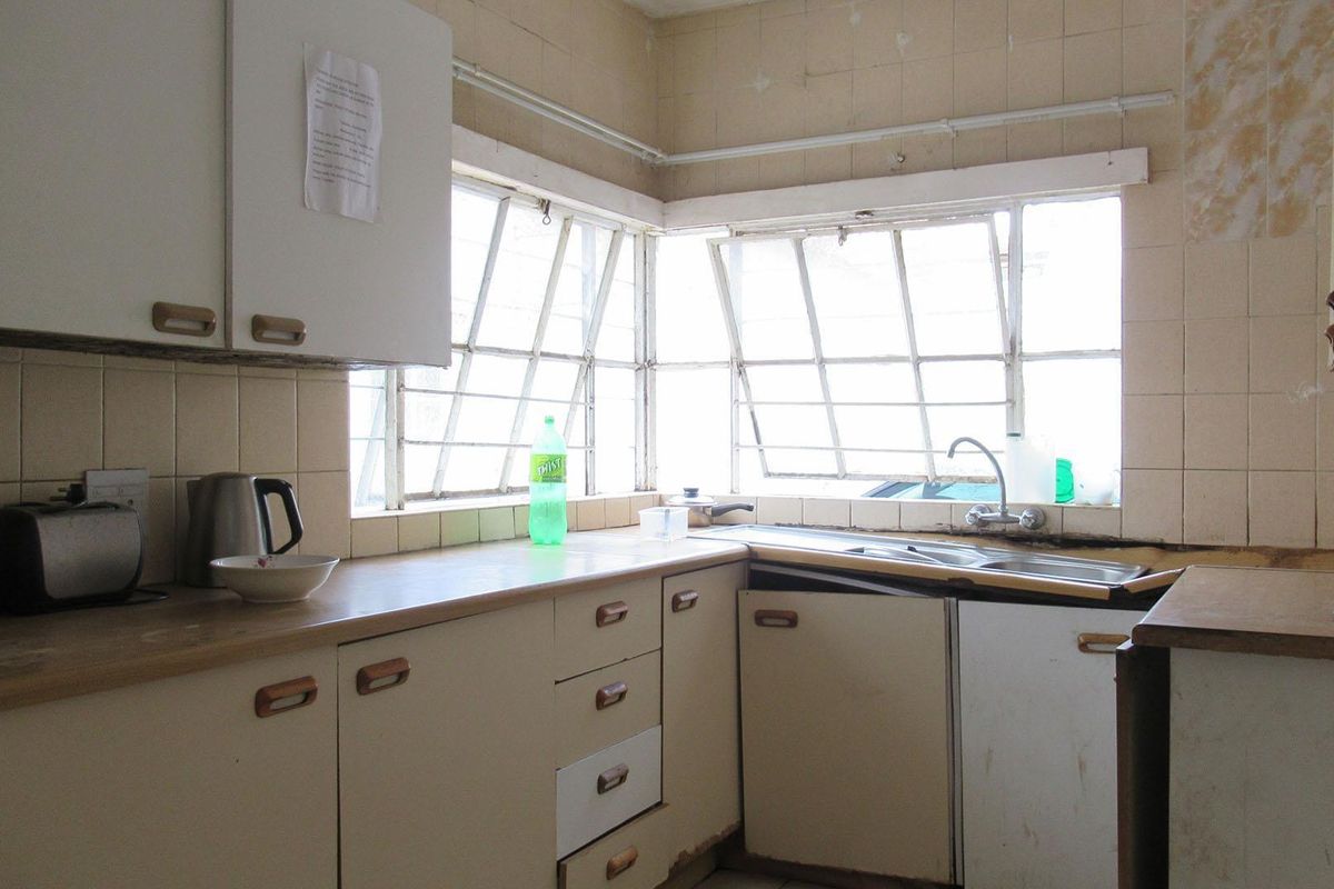 A dated kitchen featuring original cabinetry, tiled splashbacks, and corner windows, requiring significant renovation to modernize the space.