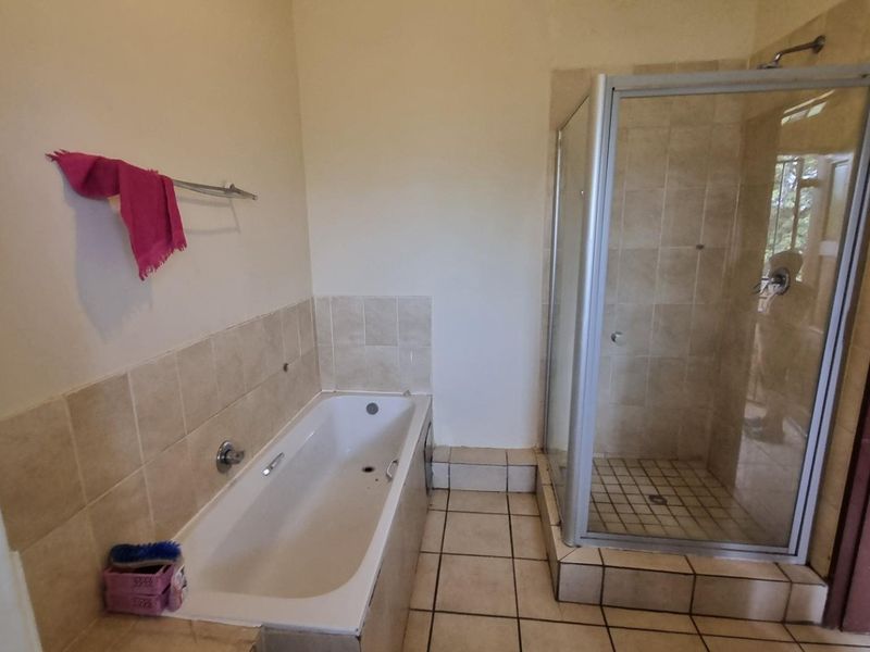 A functional bathroom featuring a built-in bathtub and a separate glass-enclosed shower with neutral tiled finishes.