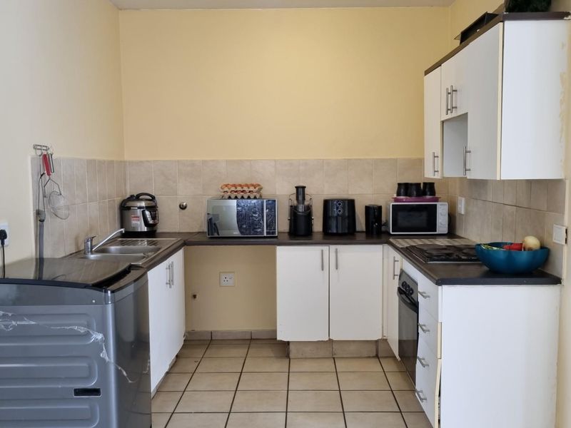 A functional kitchen featuring white cabinetry, dark laminate countertops, a tiled backsplash, and built-in cooking appliances with ceramic floor tiles.