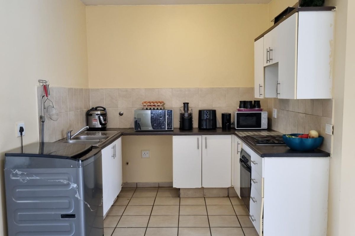A functional kitchen featuring white cabinetry, dark laminate countertops, a tiled backsplash, and built-in cooking appliances with ceramic floor tiles.