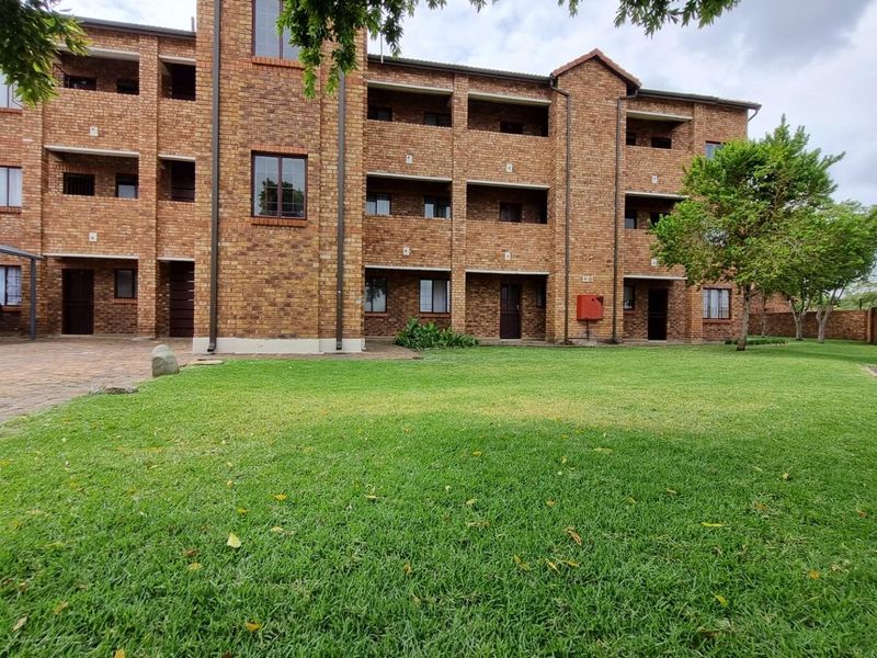 A view of the rear exterior of a multi-story face brick apartment complex featuring balconies, a paved driveway, and a well-maintained lawn.
