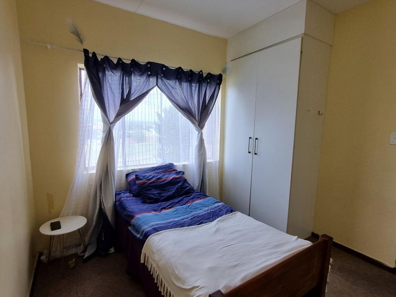 A functional bedroom featuring a built-in wardrobe, carpeted flooring, and a window providing natural light.