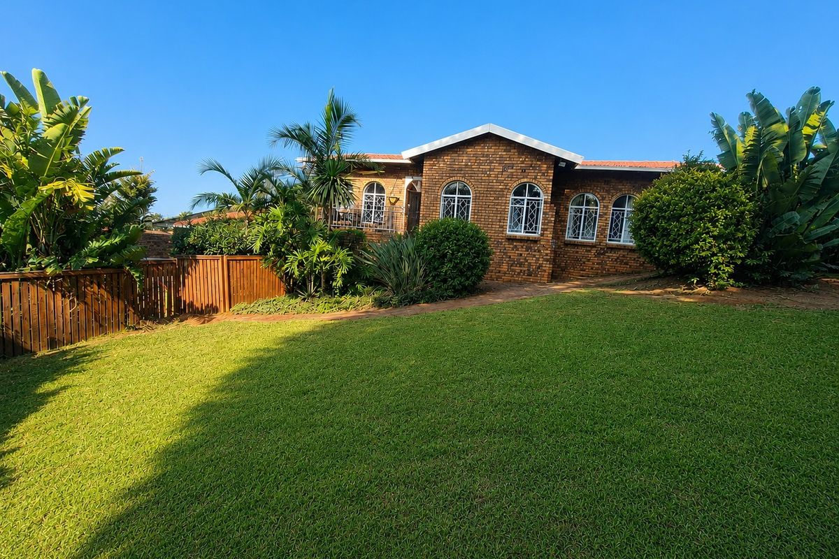 A view of the rear brick facade of the house, featuring arched windows, a well-maintained lawn, and established garden landscaping.