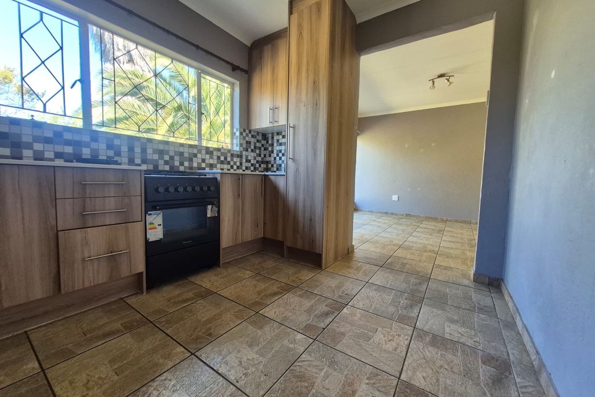 A functional kitchen featuring wood-look cabinetry, a built-in oven, and a mosaic tile backsplash, flowing into an adjacent living area with tiled flooring.