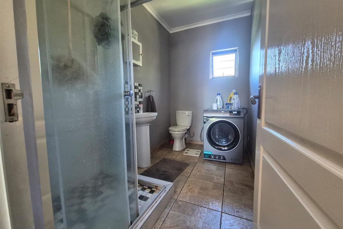 A functional bathroom featuring a glass-enclosed shower, pedestal basin, toilet, and integrated laundry space with tiled flooring.