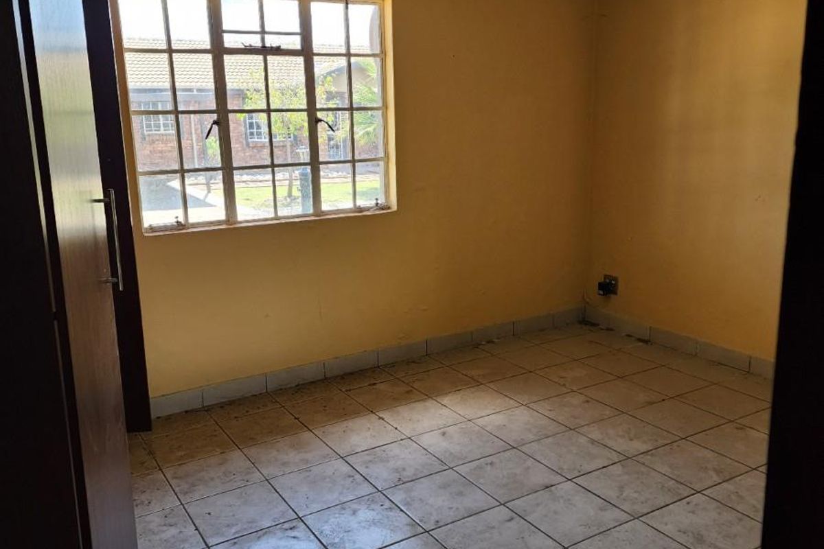A vacant bedroom featuring tiled flooring, yellow wall paint, and a window with security bars, offering a blank canvas for renovation.