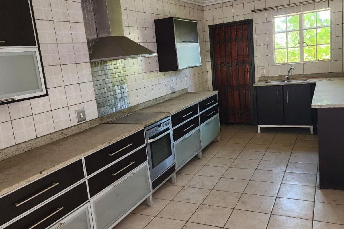 A functional kitchen featuring dark cabinetry, stone-look countertops, a built-in oven with extractor fan, and tiled flooring throughout.