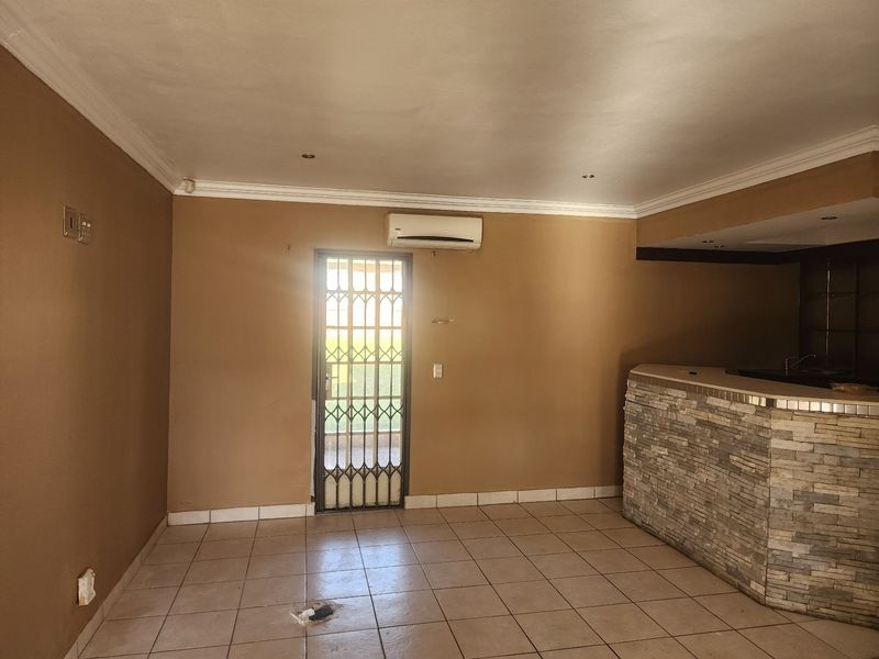 Spacious living area featuring a stone-clad built-in bar, tiled flooring, split-system air conditioning, and a secure exterior access door.
