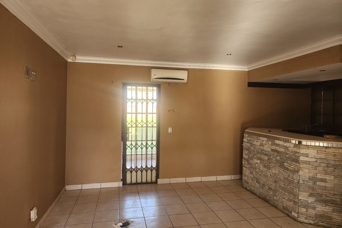 Spacious living area featuring a stone-clad built-in bar, tiled flooring, split-system air conditioning, and a secure exterior access door.