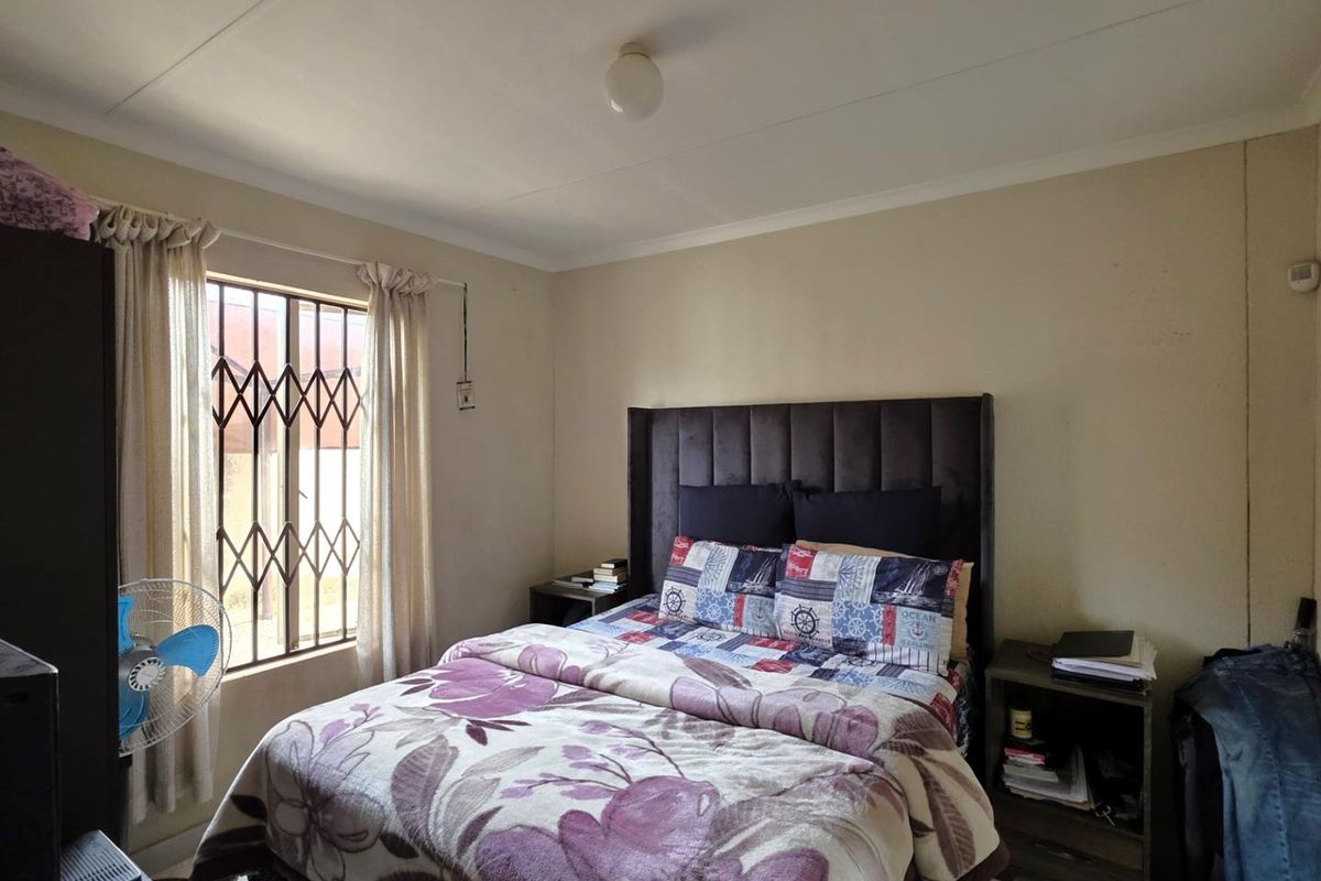 A functional bedroom featuring a window with security bars and standard ceiling lighting.