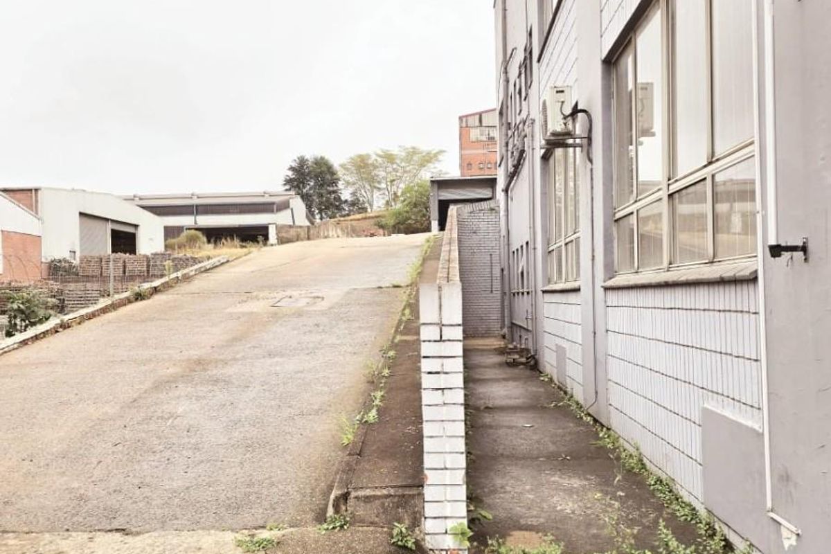 Exterior view of an industrial property showing a concrete ramp, paved walkway, and the side facade of the building structure.
