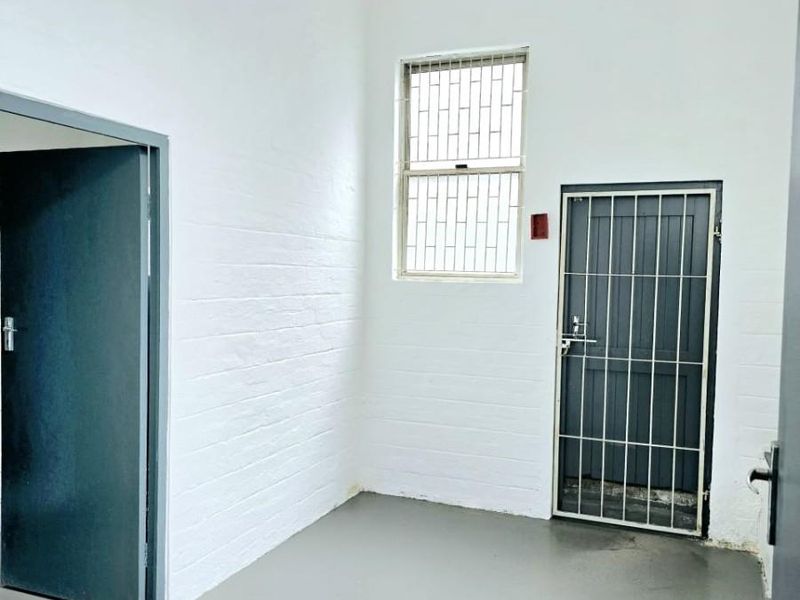 A clean, empty utility space featuring painted brick walls, a concrete floor, and secure access points with security gates and window bars.