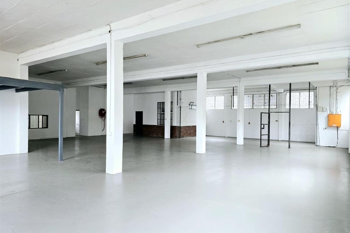 Spacious open-plan industrial warehouse area featuring high ceilings, structural columns, durable flooring, and integrated security mesh partitioning.