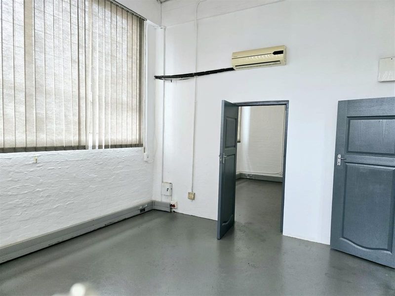 A clean, empty office space featuring painted brick walls, concrete flooring, vertical blinds, and a wall-mounted air conditioning unit.