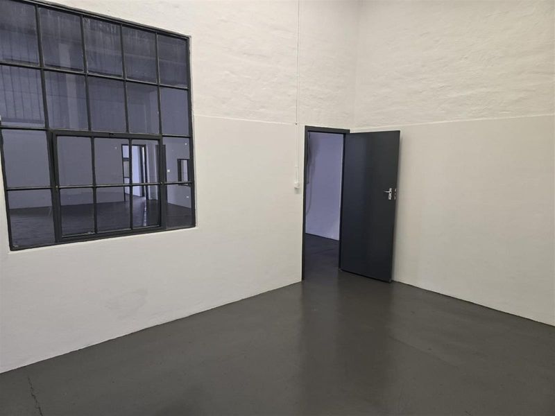 A clean, minimalist industrial utility space featuring painted concrete flooring, a large steel-framed window, and a solid interior door.