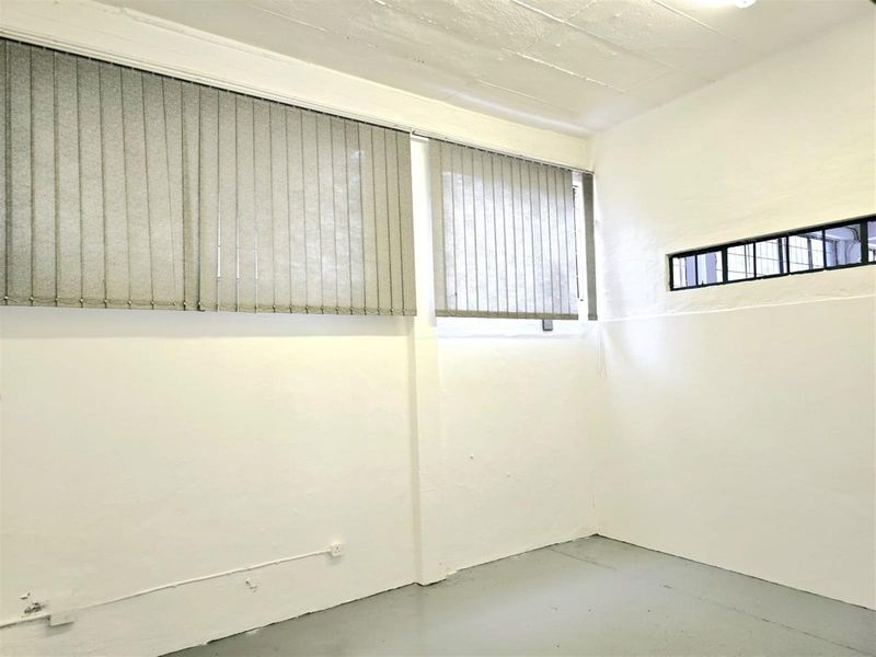 A clean, empty utility space featuring painted concrete flooring, exposed ceiling, and functional window treatments with security bars.