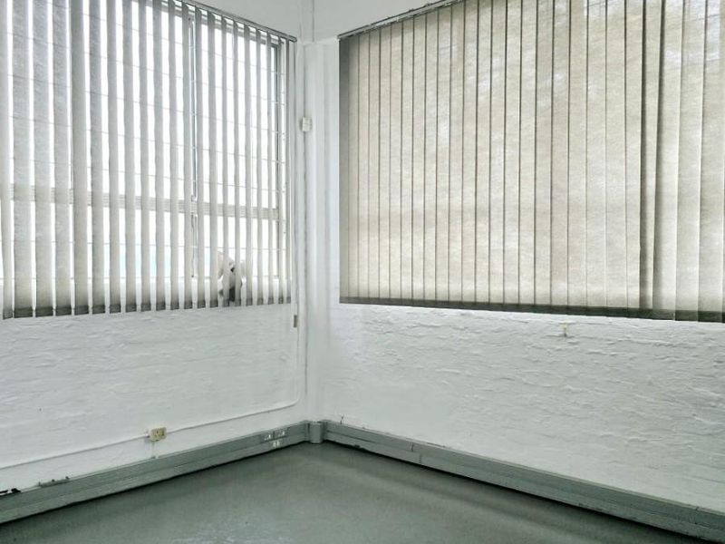A vacant industrial office space featuring painted brick walls, durable epoxy flooring, and large windows with vertical blinds, offering a functional blank canvas.