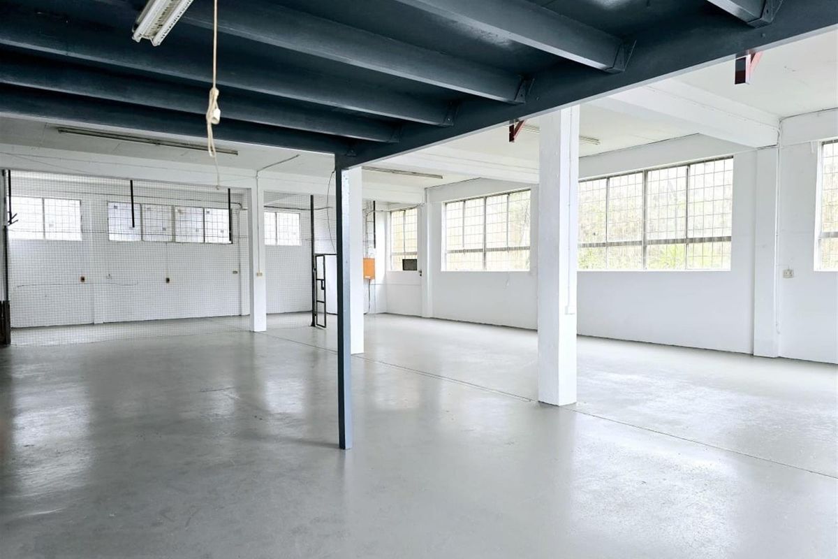 Spacious open-plan industrial unit featuring high ceilings with exposed steel beams, large steel-framed windows, and durable concrete flooring.
