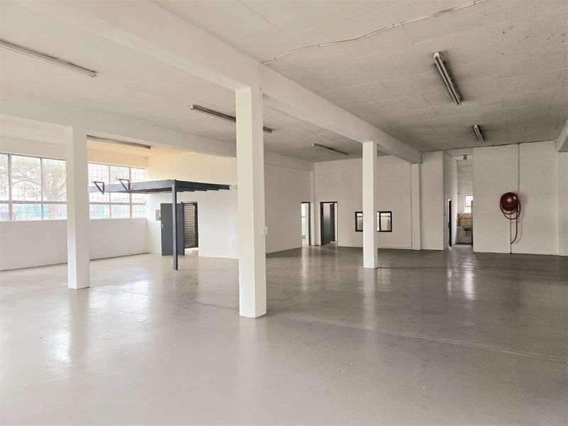 Spacious open-plan industrial warehouse area featuring concrete flooring, structural columns, mezzanine level, and functional fire safety equipment.