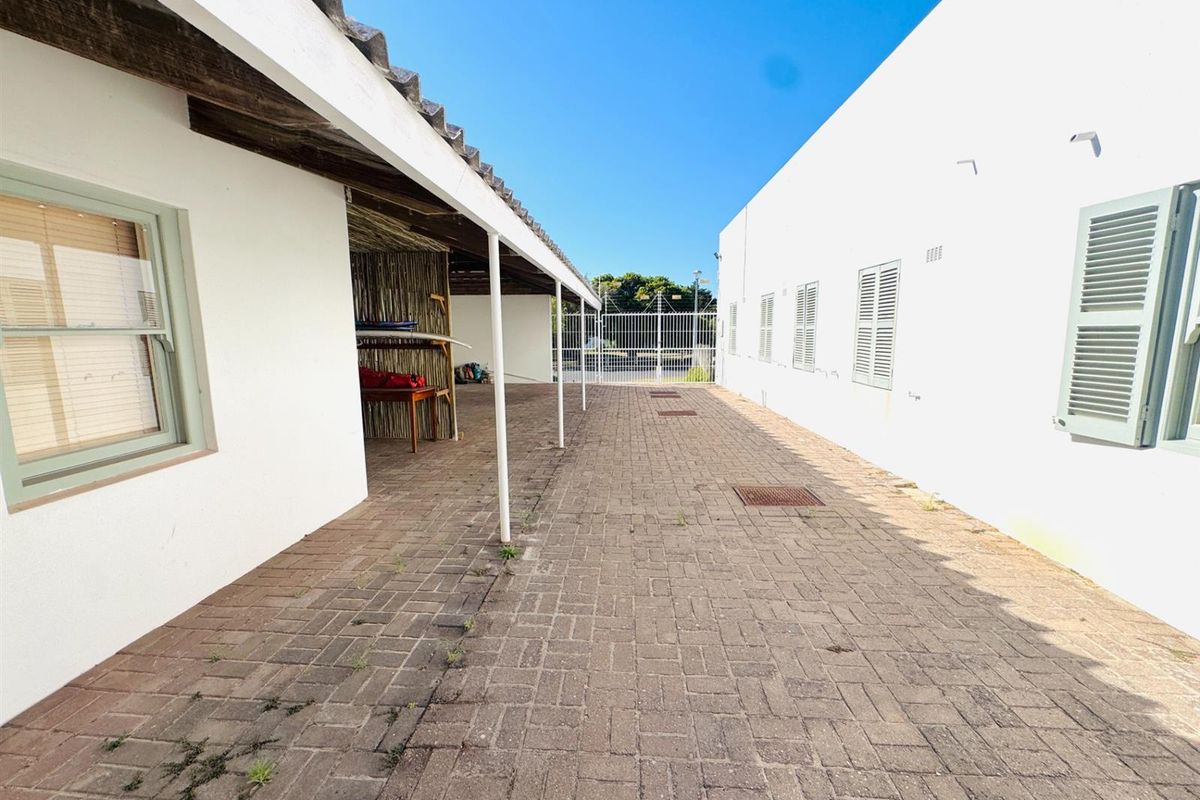 A paved outdoor walkway area between two building structures, featuring a covered patio section and secure gated access.