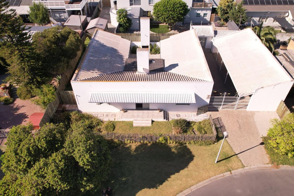 Aerial view of a detached house featuring a corrugated metal roof, central chimney, covered carport, and established garden area.