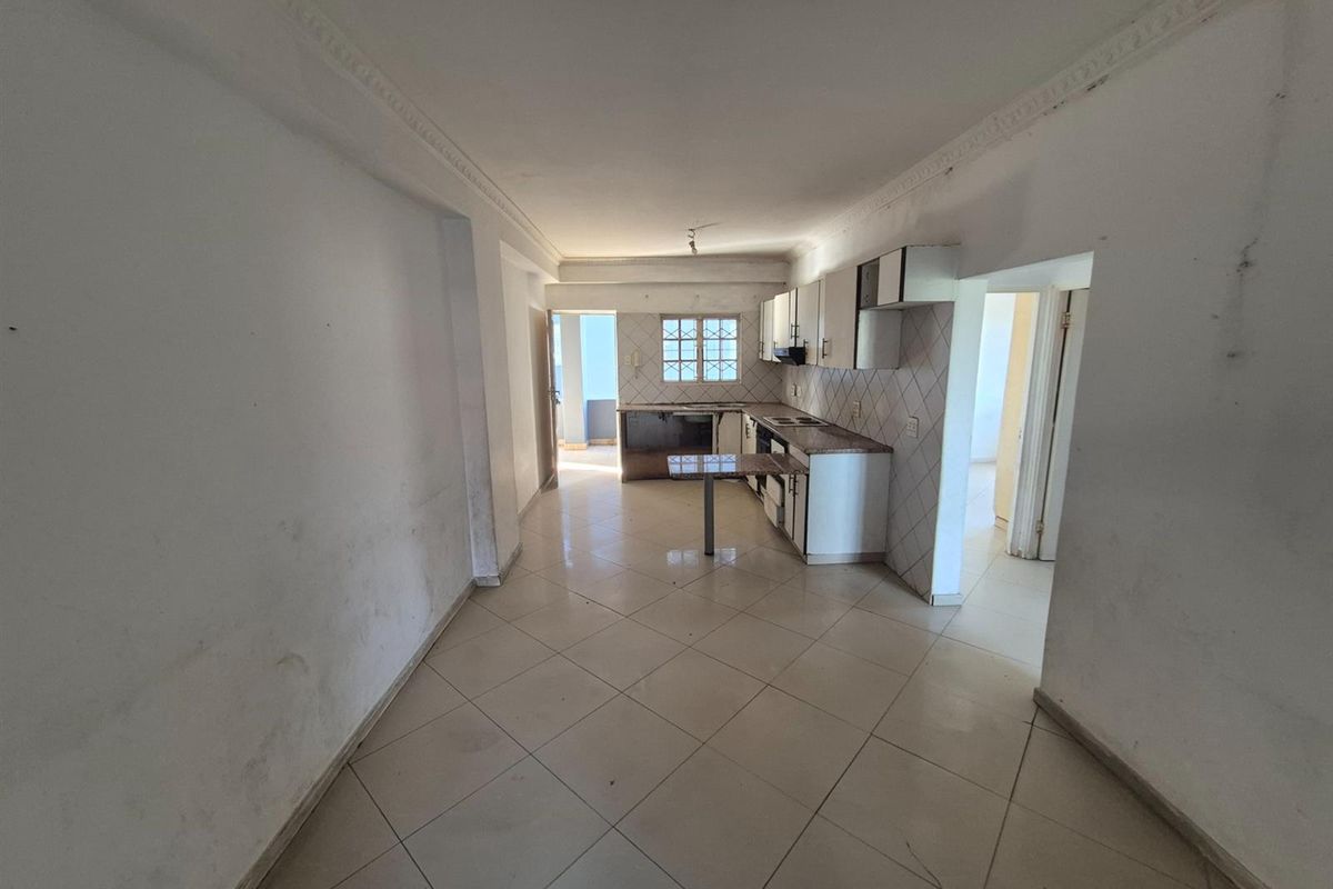 An empty kitchen featuring built-in cabinetry, tiled splashbacks, and tiled flooring, requiring cosmetic updates and wall repairs to restore its appeal.