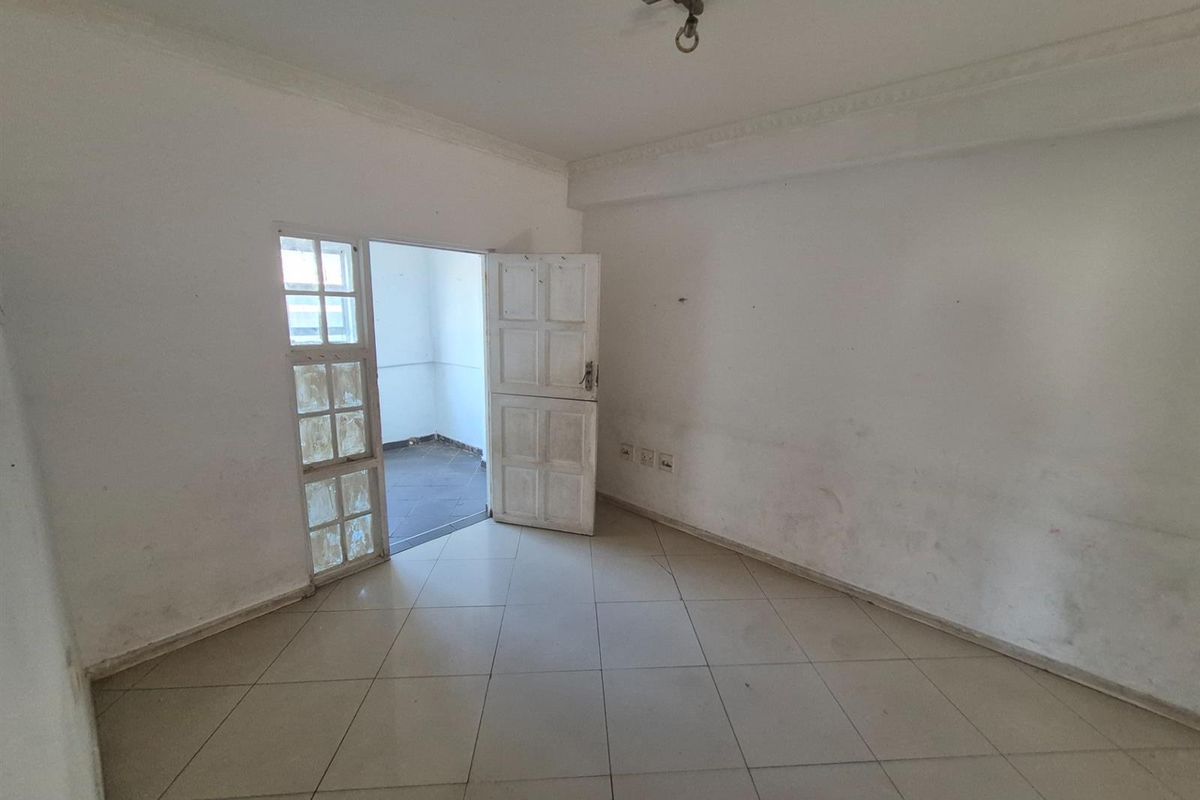 An empty living room featuring tiled flooring, coved ceilings, and access to an adjoining outdoor space through a multi-pane glass door.