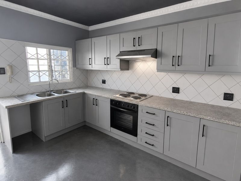 Modern kitchen featuring grey shaker-style cabinetry, granite-look countertops, built-in oven and hob, tiled backsplash, and polished concrete flooring.