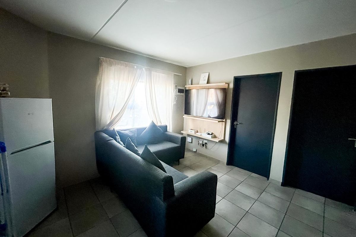 A compact living area featuring tiled flooring, neutral wall tones, and direct access to adjacent rooms via dark-finished interior doors.