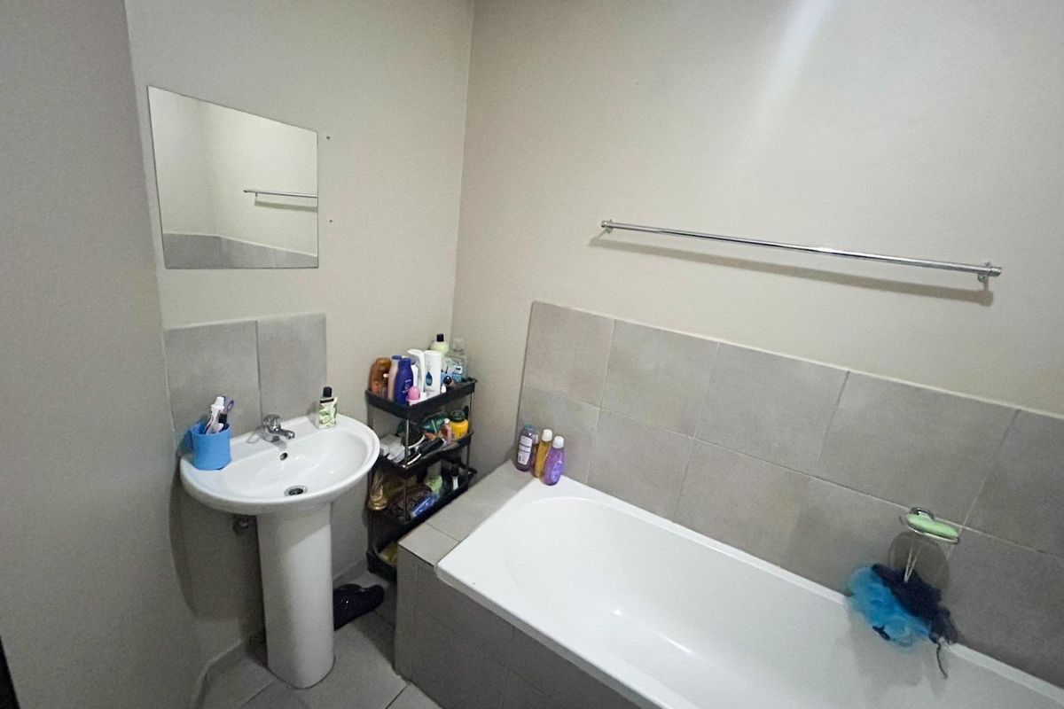 A functional bathroom featuring a pedestal basin, a tiled bathtub with a shower mixer, and a wall-mounted mirror.