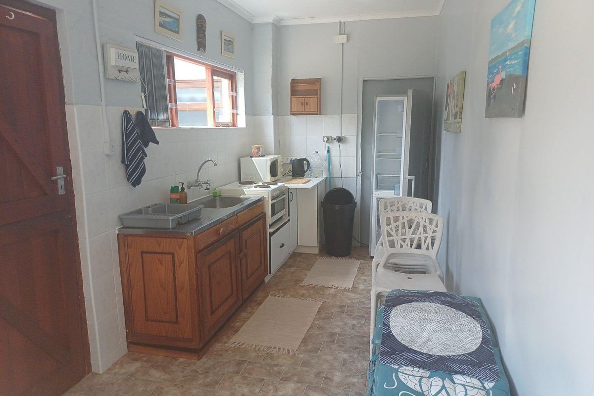 A compact kitchen featuring wooden cabinetry, a stainless steel sink, and a freestanding stove, with tiled splashbacks and vinyl flooring.