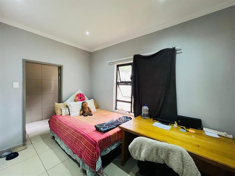 A functional bedroom featuring tiled flooring, neutral wall finishes, and a window with integrated security bars.
