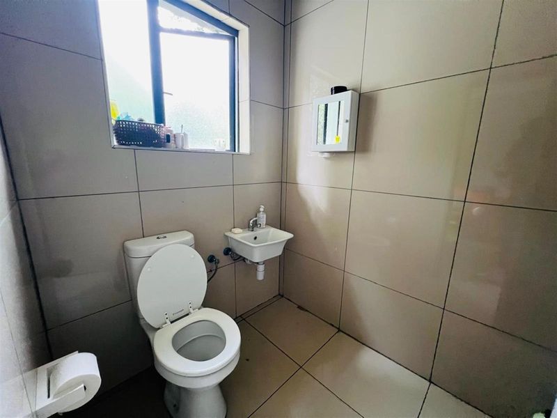 A compact guest bathroom featuring floor-to-ceiling wall tiles, a wall-mounted basin, and a standard toilet.