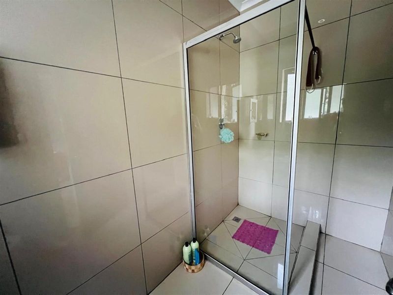 A modern bathroom shower enclosure featuring floor-to-ceiling neutral wall tiles and a glass door.