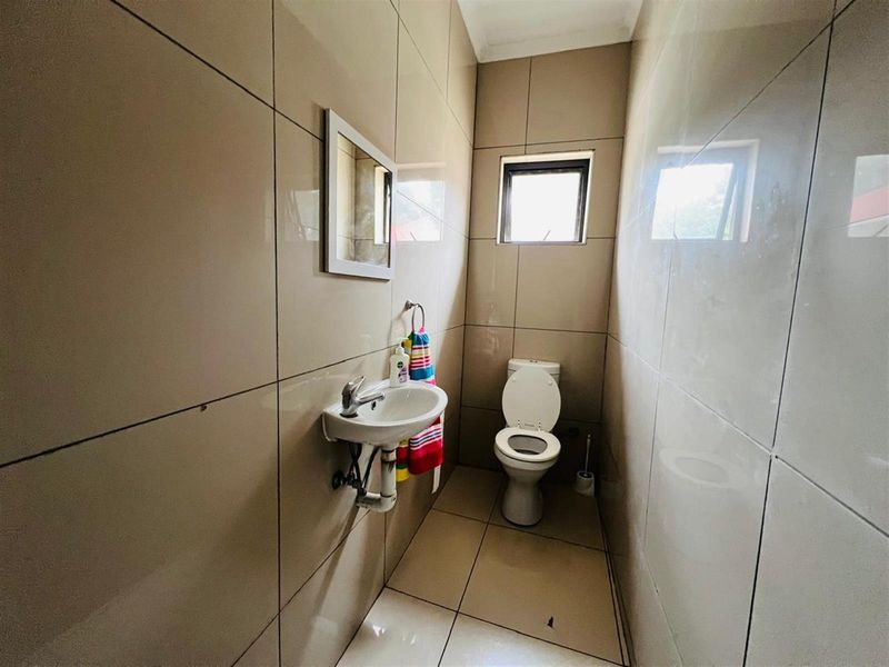 A compact guest bathroom featuring floor-to-ceiling neutral wall tiles, a wall-mounted basin, and a standard toilet.
