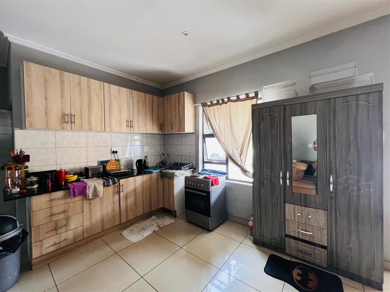A functional kitchen featuring light wood-look cabinetry, dark countertops, tiled backsplash, and a freestanding stove, with tiled flooring throughout.