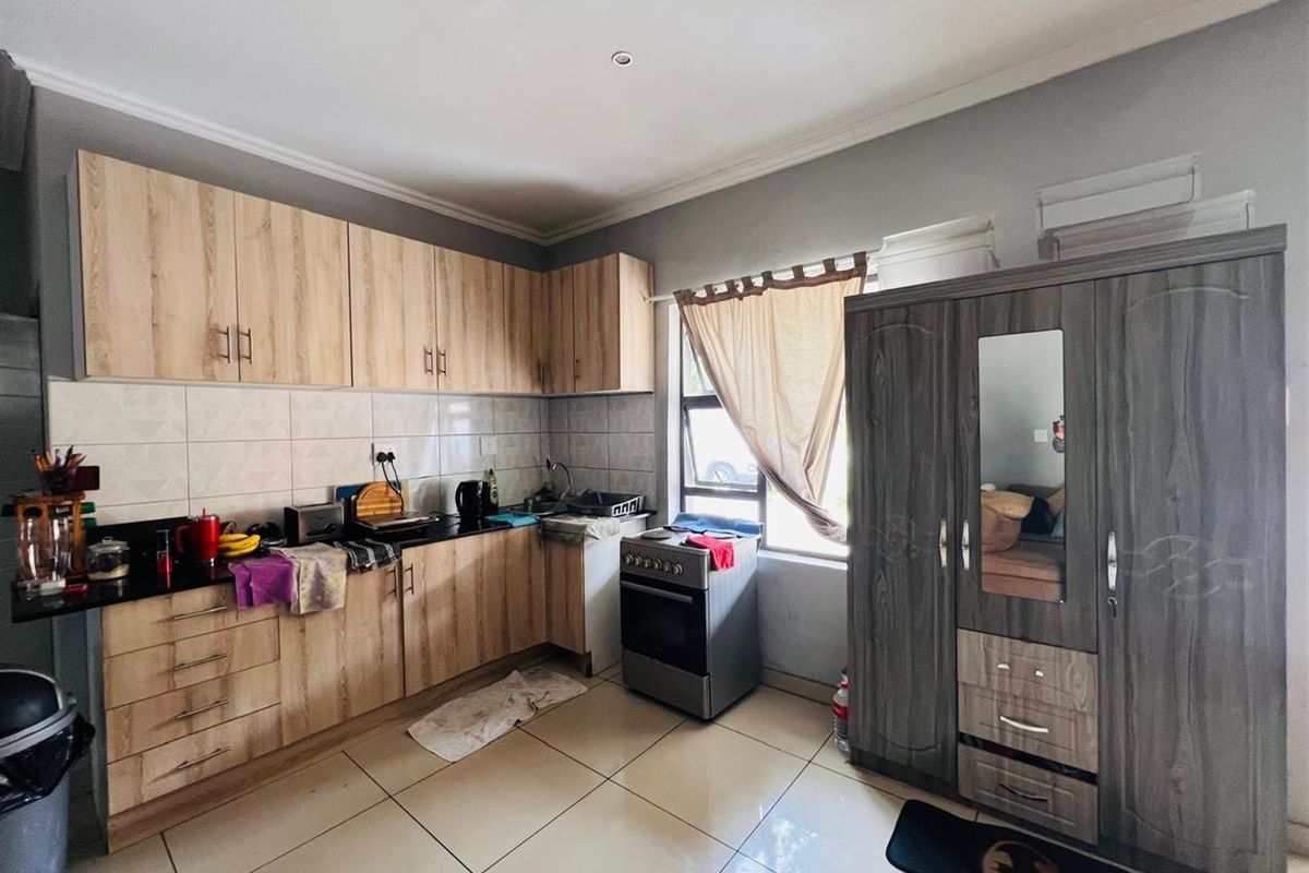 A functional kitchen featuring light wood-look cabinetry, dark countertops, tiled backsplash, and a freestanding stove, with tiled flooring throughout.