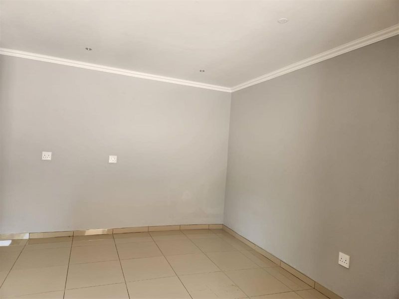 A clean, empty living area featuring neutral grey walls, tiled flooring, and recessed ceiling lighting with crown molding.