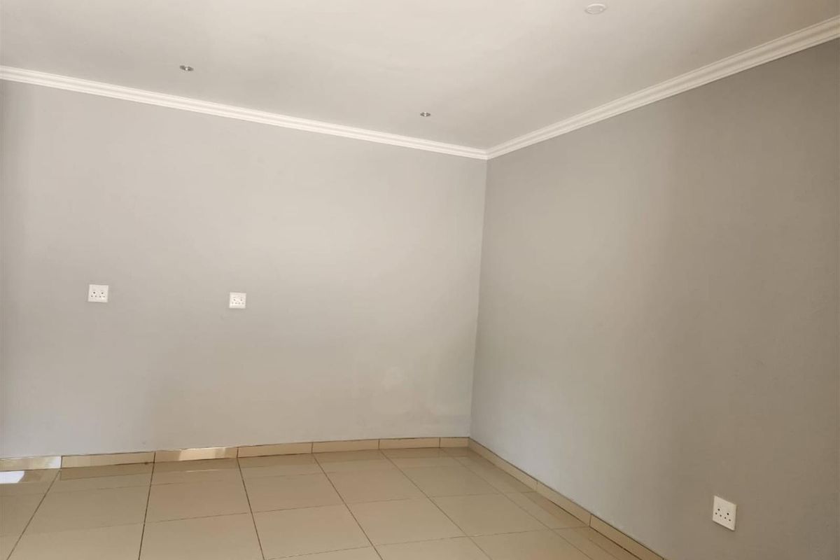 A clean, empty living area featuring neutral grey walls, tiled flooring, and recessed ceiling lighting with crown molding.