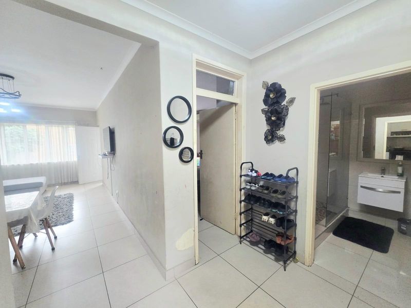 A tiled hallway connecting the living area to a bathroom featuring a modern vanity and glass shower enclosure.