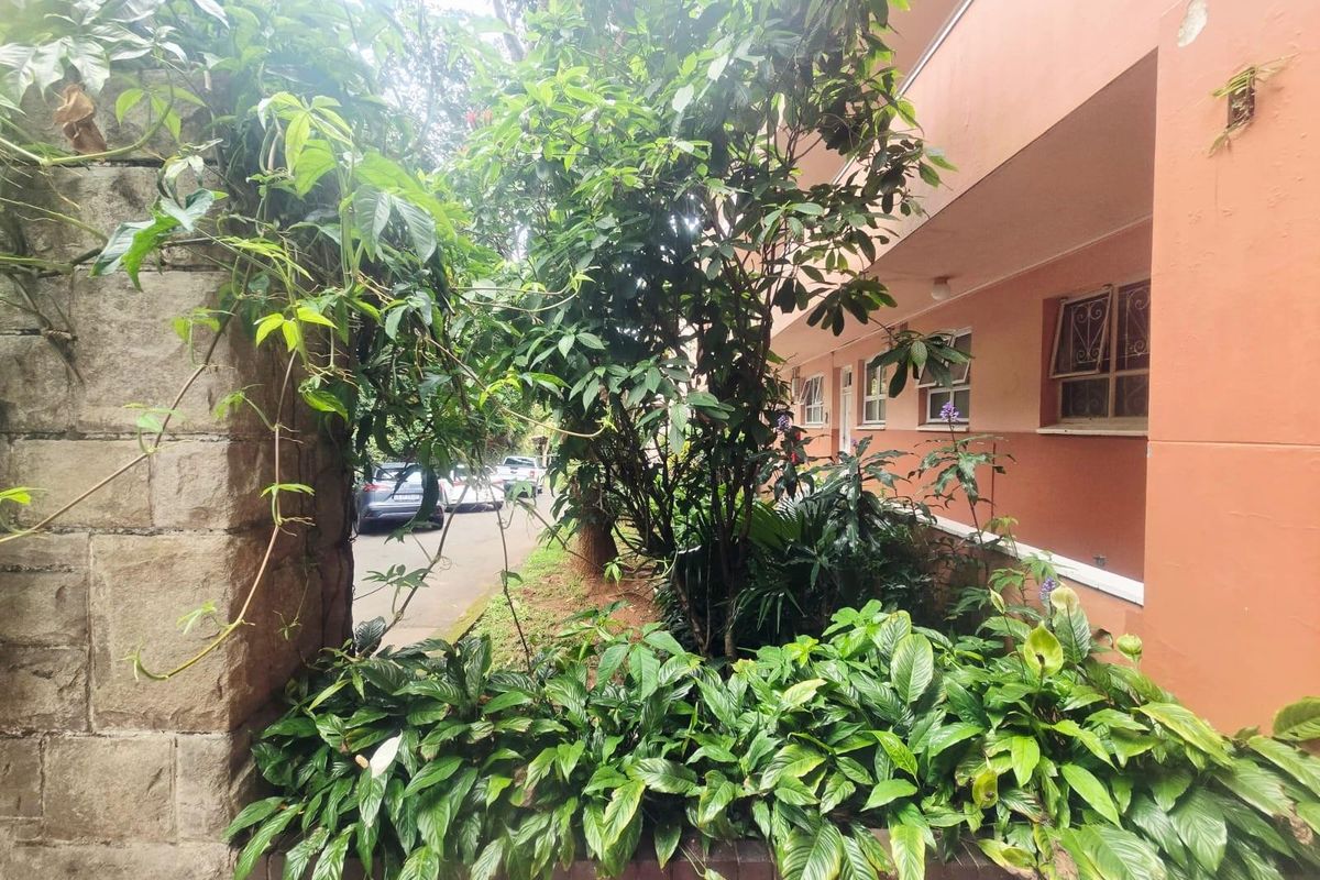 Exterior view of the apartment building facade featuring a brick retaining wall and established garden landscaping.