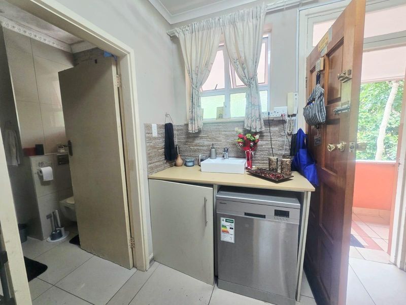 A functional laundry area featuring built-in cabinetry, a countertop with a sink, and tiled splashback, conveniently located adjacent to the bathroom.