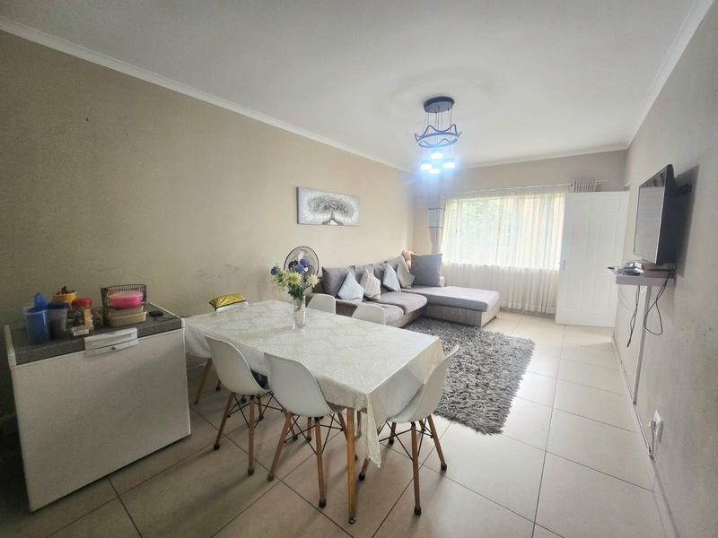 An open-plan living and dining area featuring neutral tiled flooring, cove cornicing, and a modern pendant light fixture.