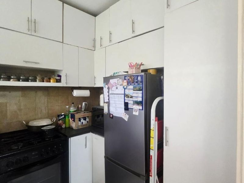 Compact kitchen featuring white built-in cabinetry, a gas stove with oven, tiled backsplash, and neutral floor tiles.