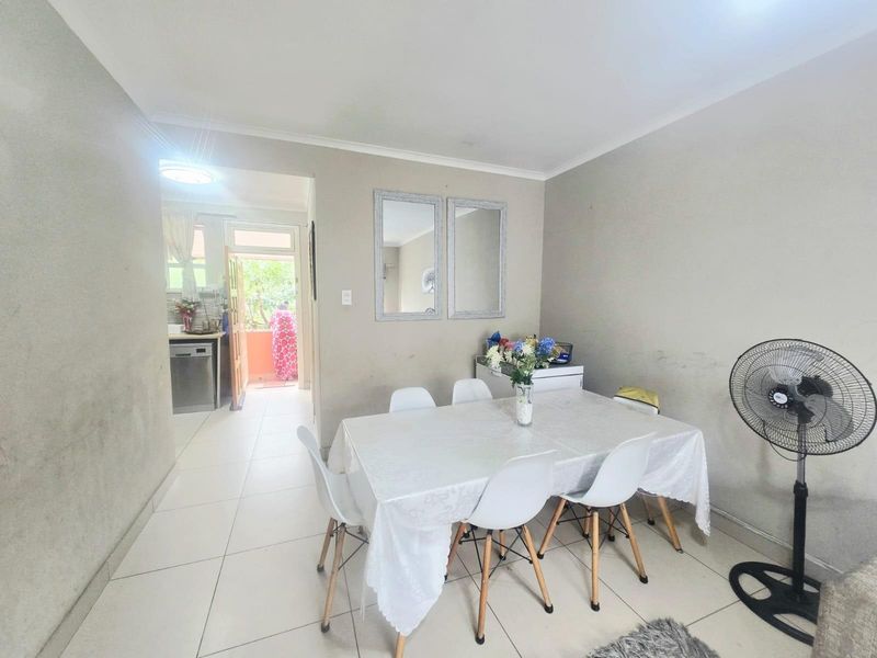 A dining area featuring tiled flooring and coved ceilings, with a view through to the kitchen and exterior entrance.