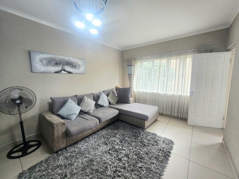 A living room featuring neutral wall tones, tiled flooring, and a window with curtain tracks, providing a functional and well-lit living space.