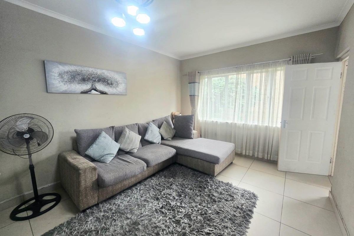 A living room featuring neutral wall tones, tiled flooring, and a window with curtain tracks, providing a functional and well-lit living space.